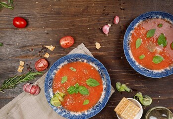 Gazpacho tomato soup in vintage blue plates on a dark wooden rough surface. Top view, horizontal with space