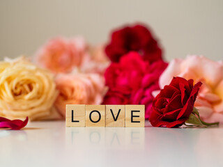 LOVE - napis z drewnianych kostek, róże w tle, różowy kolor © Klaudia Baran