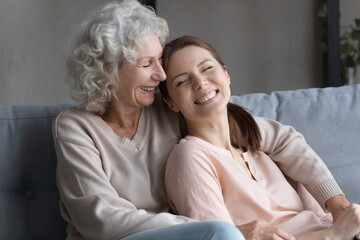 Tender moment. Smiling millennial woman grown up child daughter of senior female sit on couch lean...