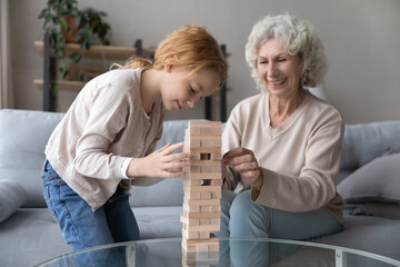 Mu turn, granny. Focused little school age girl play logic game with mature grandma build tower...