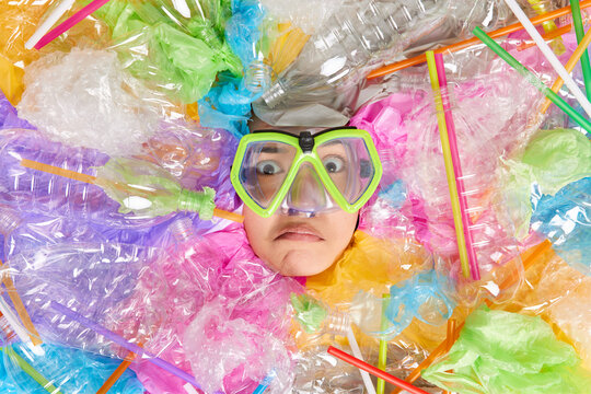 Ecology eco lifestyle and protection on earth concept. Worried displeased woman sticks head through plastic wastes wears big snorkeling glasses poses among trash collects litter for recycling.