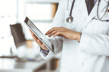 Unknown male doctor using tablet computer in clinic near his working place, closeup. Perfect medical service in hospital. Medicine and healthcare concept