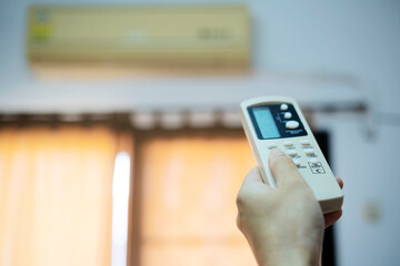 Hand holding remote control, adjusting temperature of air conditioner