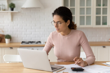 Focused millennial hispanic caucasian woman in eyeglasses calculating domestic expenses, paying...