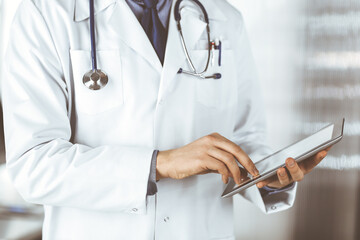 Unknown male doctor using tablet computer in clinic near his working place, closeup. Perfect medical service in hospital. Medicine and healthcare concept