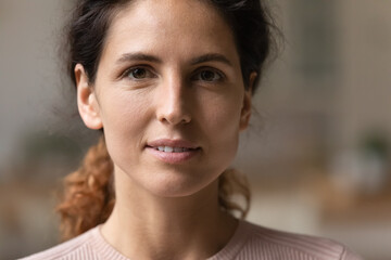 Close up head shot view attractive young 30s authentic woman with perfect skin looking at camera. Portrait of happy pleasant millennial caucasian hispanic latin confident lady with natural beauty.