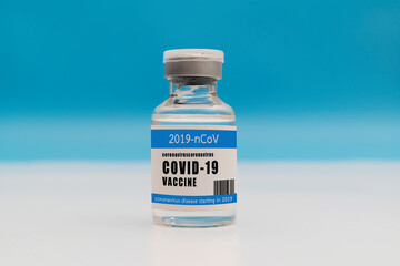 Vial of Covid - 19 vaccine against blue background.