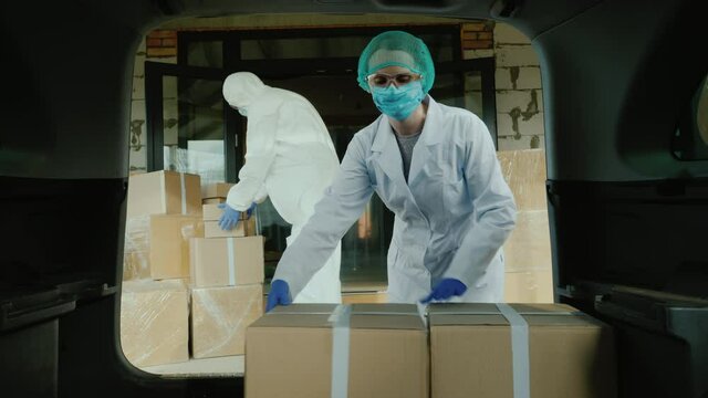 Men movers in protective suits load cardboard boxes with medicines into the car