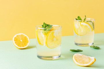Fruit water with lemon and mint leaves on combined yellow and green background. Two glasses of cool carbonated cocktail with citrus. - obrazy, fototapety, plakaty