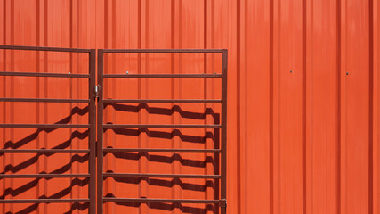 Open brown folding metal garage gate on orange corrugated steel wall background