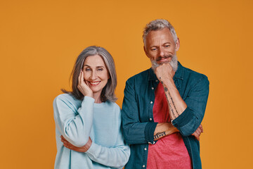 Beautiful senior couple smiling while standing together against orange background