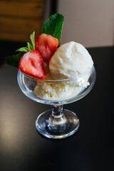 three white balls of ice cream in a glass cup or a bowl, a glass. Red strawberries cut in two with green petals as an ice cream decoration