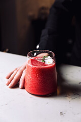 Bartender holding a glass of refreshing strawberry and banana smoothie cocktail garnished with an edible flower, marble table.