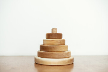 Modern natural wooden pyramid with rings on table on white wall background. Eco friendly plastic free toys for toddler. Stylish simple wooden toy for child. Space for text. Montessori education