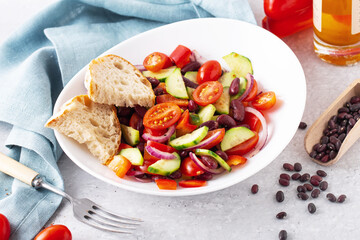 spanish salad with red beans and vegetables in a white plate, light blue napkin, tomatoes, cucumbers, onions, ciabatta