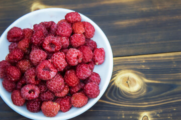 Ripe raspberries on a white plate on a wooden background. Summer