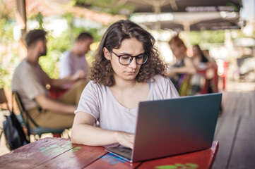 Freelancer woman sitting in cafe on street and working on laptop. Internet connection, networking. Device electronics gadget concept