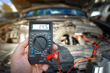Man test car alternator and check car battery voltage with multimeter on start engine. Measuring voltage on car battery. Voltmeter for service maintenance, prepare car battery for cold season - obrazy, fototapety, plakaty