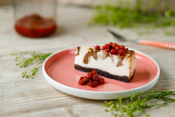 Cheesecake with chocolate flavor lies on a plate with wild strawberries on a wooden table. 