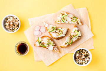 Ready-to-eat bruschetta with curd cheese, cucumber, radish and sprouted grains on paper on a yellow background. Healthy snacks. Top view