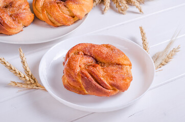Fresh tasty cinnamon sugar bun on white plate on wooden background