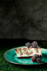 Cheesecake with chocolate flavor is on a plate with blackberries.
