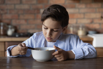 Serious focused boy kid having breakfast in kitchen, sitting at table, eating cereals, morning...