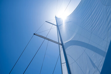 Yacht sails on clear blue sky background. Sailing with the wind at open sea ocean, summer holidays