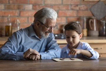 Happy grandpa and little grandson engaged in learning board game, grandfather teaching kid to play...