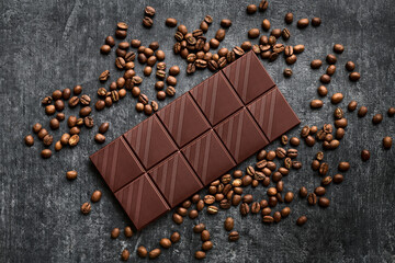 Chocolate bar in a scattering of coffee beans, dark, top view, close up