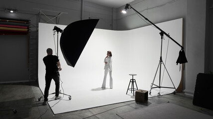 Fashion photography in a photo studio. Professional male photographer taking pictures of beautiful woman model on camera, backstage