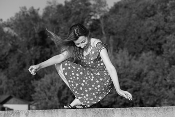 Naklejka premium Beautiful woman in summer dress sitting on concrete fence in black and white