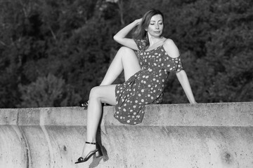 Beautiful woman in summer dress sitting on concrete fence in black and white