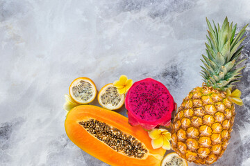 Ripe pineapple, papaya, dragon fruit, passion fruit and flowers on a gray marble background. Flat lay, food concept.