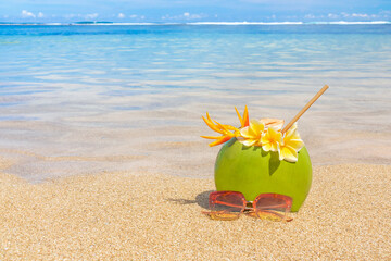 Fresh coconut juice with sunglasses on the background of a beautiful beach.
