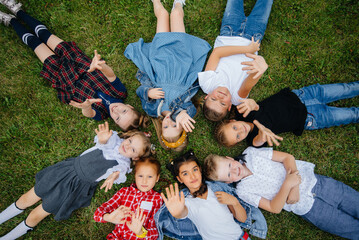 A group of school children lie on the grass in a circle and have fun. Happy childhood