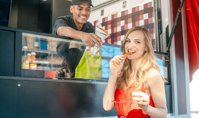 Beautiful woman ordering fries at a food truck taking a first bite