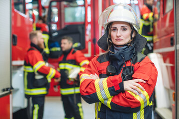 Beautiful fire fighter woman with her helmet in hand standing in the firehouse - 443296108