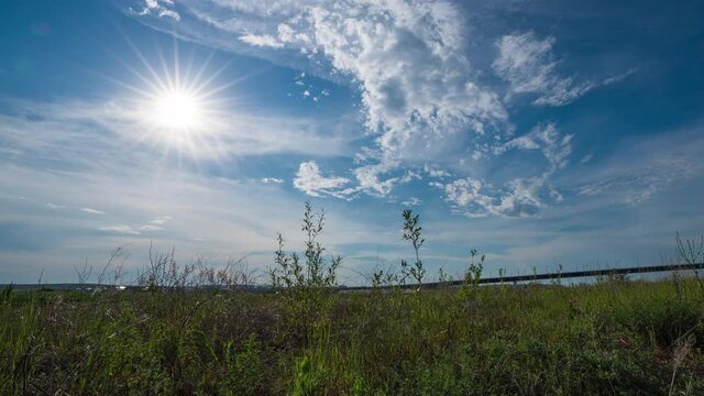 Time lapse of movement of white clouds across the blye sky. Sunset, in the evening. The movement of the camera in the grass above the river. 4K Hyperlapse