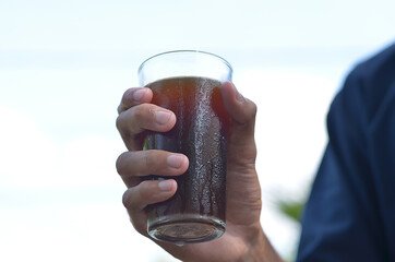 male hand holding Iced Coffee in the glass refreshing look with blurred background. selective focus