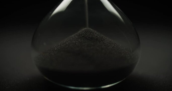 Macro shot of black sand falling in reverse inside a transparent sand glass. Reverse time concept. 