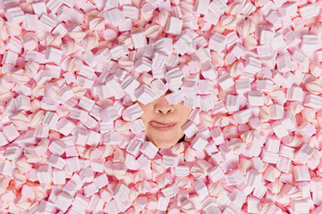 Unrecognizable woman buried in marshmallow licks lips wants to eat delicious dessert has sweet...