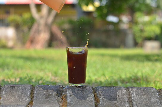 ice cube falling to Iced Coffee in the glass refreshing look with blurred background. selective focus