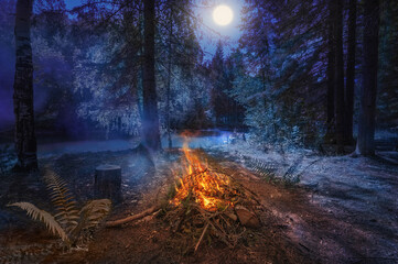 At night, a bonfire burns on the river bank in the forest, next to a fern bush is a symbol of the pagan holiday of Ivan Kupala. The full moon is shining.