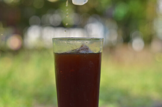 ice cube falling to Iced Coffee in the glass refreshing look with blurred background. selective focus