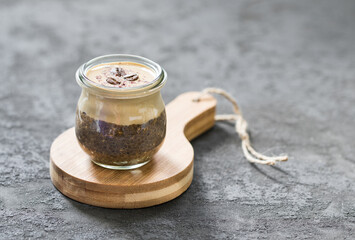 Coffee pudding chia seeds with cottage cheese cream in a glass jar on a wooden board on a dark gray background