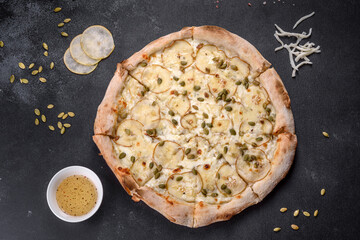 Fresh delicious Italian pizza with pear and pumpkin seeds on a dark concrete background