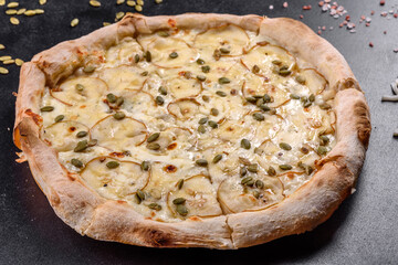 Fresh delicious Italian pizza with pear and pumpkin seeds on a dark concrete background