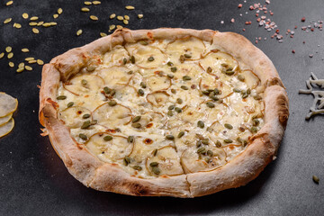 Fresh delicious Italian pizza with pear and pumpkin seeds on a dark concrete background