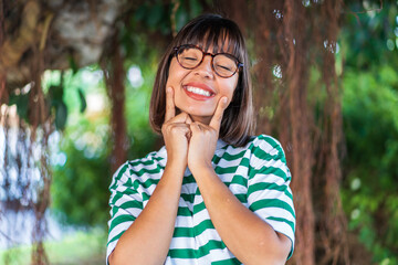 Young brunette woman at outdoors in a park smiling with a happy and pleasant expression
